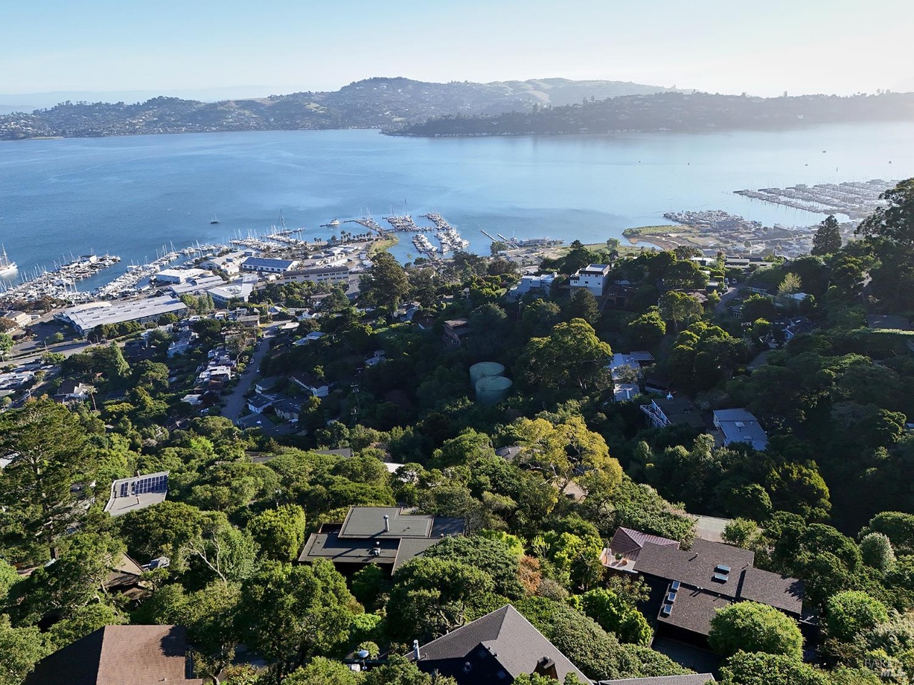 An aerial view of the wooded Sausalito hillside above Richardson Bay, the marina and harbor below and the Marin headlands across the water
