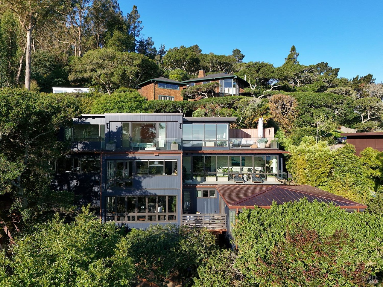 The full massing of 234 Currey Lane built into the hillside, multiple glass-walled levels and terraces with a copper roof, surrounded by mature greenery