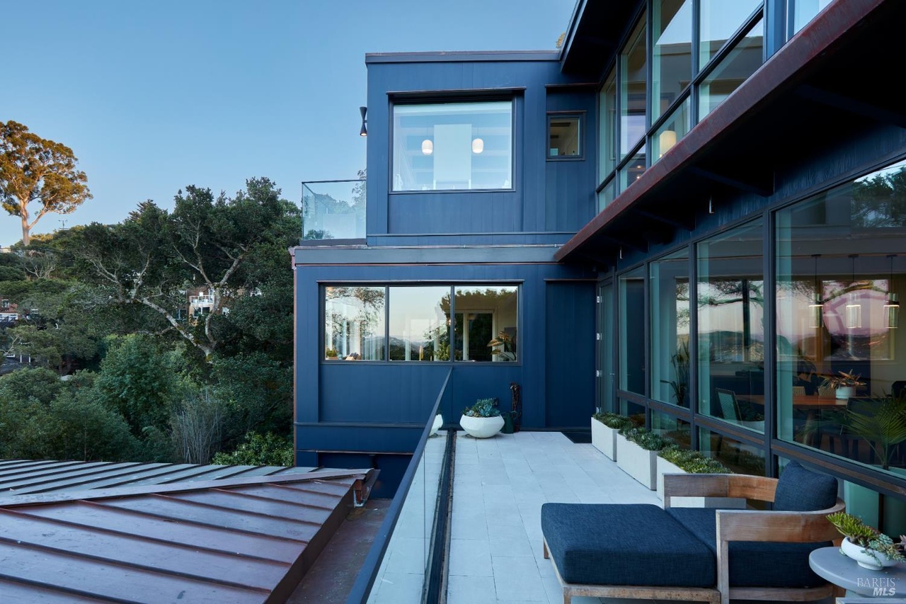 The deep-blue board-and-batten facade of 234 Currey Lane at golden hour, walls of glass and a copper roofline above a terrace with chaise lounges on a Sausalito hillside